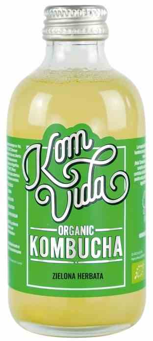 Bio Grüner Tee Kombucha von KOMVIDA in 250ml Flasche mit sprudelnder Textur und grünen Teeblättern im Hintergrund